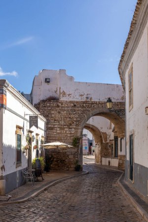 Foto de Faro, Portugal - October 3, 2020: old cobble stone street in the old town of Faro with traditional narrow small houses and white painted walls in Portugal. - Imagen libre de derechos
