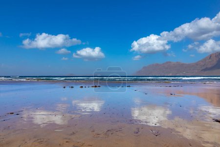 Foto de Playa de arena escénica en Famara en Lanzarote con reflejo en el agua de las nubes - Imagen libre de derechos