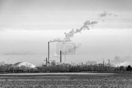 Photo for Industry complex in Frankfurt in late evening with  fields and smoking chimney in winter - Royalty Free Image