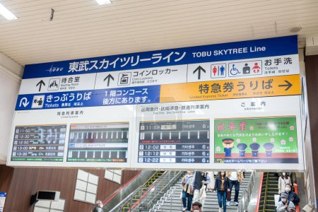 Foto de Tokio, Japón - 17 de marzo de 2023: personas en la estación de metro de Tokio. Señalización en japonés e inglés muestran a los turistas la dirección y el horario del metro. - Imagen libre de derechos