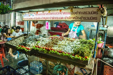 Foto de Bangkok, 6 de mayo de 2009: mujer con su restaurante callejero vende verduras frescas, fideos y té en su cabina nocturna en la calle. Ella cocina con Gas. - Imagen libre de derechos