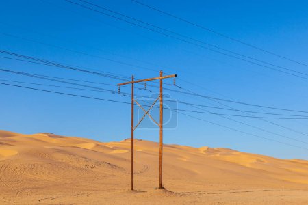 Foto de Pilón eléctrico en el desierto con pila de madera bajo el cielo azul - Imagen libre de derechos
