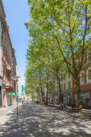 Foto de Wiesbaden, Alemania - 18 de mayo de 2023: calle peatonal al sol del mediodía con árboles y tiendas en los edificios históricos clasicistas. - Imagen libre de derechos