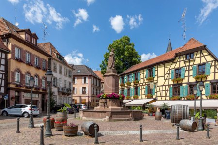 Photo for Ribeauville, France - June 23, 2023: A picturesque colorful street of half-timber buildings with shops and cafes in the village of Ribeauville, in the Alsace region. - Royalty Free Image