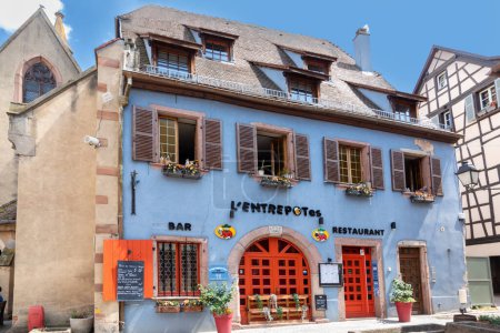 Foto de Ribeauville, Francia - 23 de junio de 2023: Una pintoresca calle colorida de edificios de media madera con tiendas y cafeterías en el pueblo de Ribeauville, en la región de Alsacia. - Imagen libre de derechos