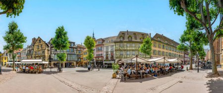 Foto de Colmar, Francia - 21 de junio de 2023: Plaza Dominicana en Colmar, Francia con casas de madera y turistas, disfrutando sentados en los cafés en un día de verano. - Imagen libre de derechos