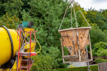 Téléchargez les photos : Détail de bétonnière et vanne sur une grue sur un chantier iavec des arbres en arrière-plan - en image libre de droit