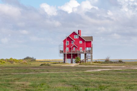Photo for New beach house in red  at Port Bolivar on wooden stilts to protect against flooding, Texas, USA - Royalty Free Image
