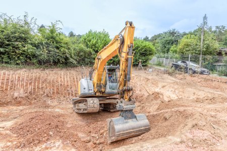 Photo for Fischbach, Germany - July 15, 2020: large digger digs a hole for the cellar of a family house,the worker checks the distance and heigh of the excavation pit - Royalty Free Image