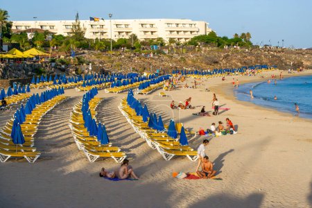 Foto de Playa Blanca, España - 5 de agosto de 2007: la gente disfruta de la playa con salones de playa y sombrilla en Playa Blanca, hotel de fondo, Lanzarote, España - Imagen libre de derechos