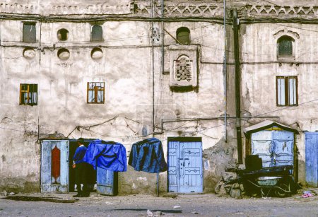 Téléchargez les photos : Sanaa, Yémen - 30 juin 1991 : vieux mur de maison dans la ville de Sanaa au Yémen dans un aerea pauvre avec des portes bleues typiques. - en image libre de droit