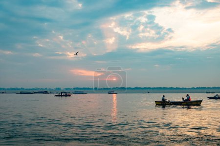 Téléchargez les photos : Vieux bateaux en bois sur le fleuve Ganges avec des touristes à bord pour regarder le lever du soleil pittoresque à Varanasi et le culte burnig des morts - en image libre de droit