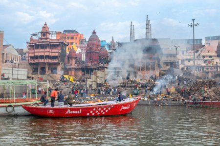 Téléchargez les photos : Varanasi, Inde - 24 février 2024 : vieux bateaux en bois à la jetée à la frontière de la rivière Ganges dans la lumière du matin avec des gens sur la jetée à Varanasi. - en image libre de droit