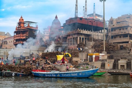 Téléchargez les photos : Varanasi, Inde - 24 février 2024 : vieux bateaux en bois à la jetée à la frontière de la rivière Ganges dans la lumière du matin avec des gens sur la jetée à Varanasi. - en image libre de droit
