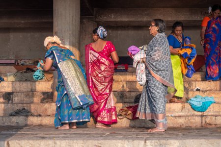 Téléchargez les photos : Varanasi, Inde - 24 février 2024 : de belles femmes habillées après un bain dans la rivière du Gange entrent dans un hospice à la banque du Gange à Varanasi, en Inde. - en image libre de droit