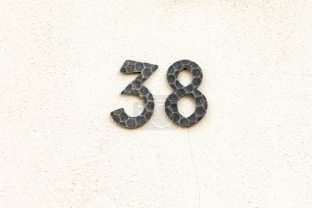 Hausnummer 38 aus Metall an weiß gestrichener Putzwand im Vintage-Stil