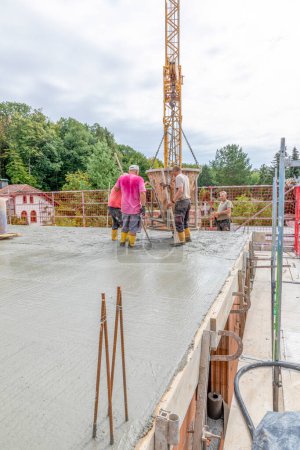 Photo for Fischbach, Germany - August 25, 2020: worker at the construction site pouring a foundation of a family house with concrete mixer and scaffold. - Royalty Free Image