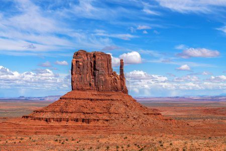 Merrick Butte in Monument Valley framed against a beautiful, vibrant blue sky with puffy white clouds.
