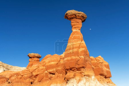 Weißer und roter Sandstein-Fliegenpilz-Hoodoo bei Kanab Utah mit stark erodierten Kirchtürmen und ausbalanciertem härterem Fels auf der Spitze, eingerahmt von blauem Himmel.
