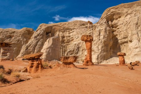 Weißer und roter Sandstein-Fliegenpilz-Hoodoo bei Kanab Utah mit stark erodierten Kirchtürmen und ausbalanciertem härterem Fels auf der Spitze, eingerahmt von blauem Himmel.