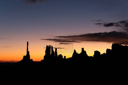 Sunrise behind Monument Valley's famous totem pole and nearby spires, all formed by millions of years of erosion from wind and rain.