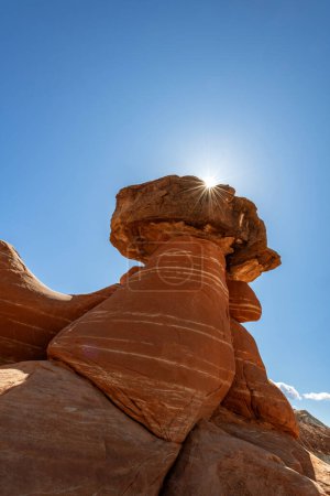 Beautiful Toadstool Hoodoos in Kanab Utah shows a backlit image with a sunburst of light framing the eroded formation.  The sandstone is harder on the top and softer below the cap, causing this unique rock structure. 