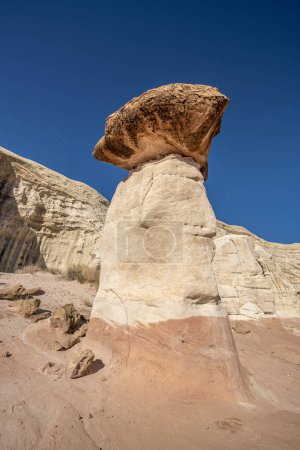 White and red sandstone toadstool hoodoo at Kanab Utah highlighted by blue sky and a white low mountain range.