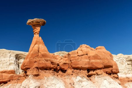 White and red sandstone toadstool hoodoo at Kanab Utah showing highly eroded spires and balanced harder rock on top framed by a blue sky.