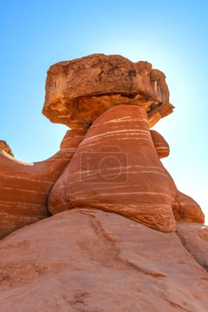 Weißer und roter Sandstein-Fliegenpilz-Hoodoo bei Kanab Utah mit stark erodierten Kirchtürmen und ausbalanciertem härterem Fels auf der Spitze im Gegenlicht der Sonne und des strahlenden Himmels.