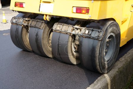 Téléchargez les photos : Rouleau pneumatique de pneus compactant l'asphalte neuf d'une rue. Repavage de la chaussée. Travaux routiers - en image libre de droit