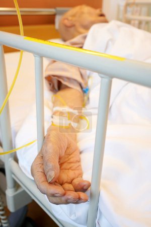 Téléchargez les photos : Gros plan de la main du patient âgé avec goutte à goutte intraveineuse au lit de l'hôpital - en image libre de droit