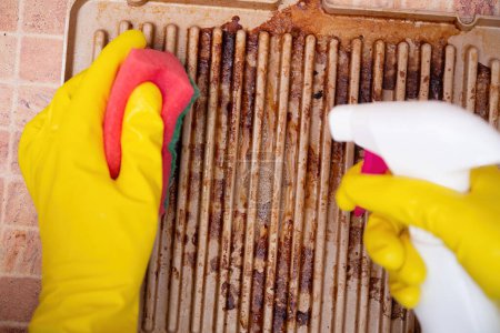 Photo for Man cleaning grilled pan or electric grill with detergent agent. Hands in yellow gloves clean grill burned and grease dirt after barbeque - Royalty Free Image