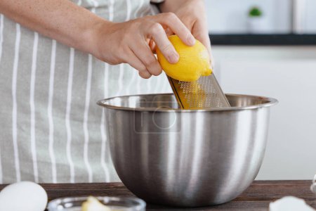 The cook's hands grate the zest of a lemon into a bowl of dough. Natural flavor in vidi lemon zest. Preparing ingredients in a bakery or restaurant kitchen