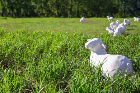 White, life-sized sheep sculptures rest in a lush green meadow