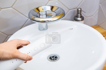Hand activating a water flosser with a jet of water in a chic bathroom, emphasizing oral cleanliness and care.