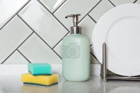 Soap dispenser and sponges beside clean dishes or white plates. Home hygiene and dish washing, home decor