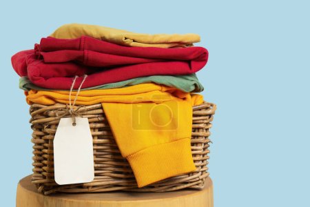 Colorful folded clean clothes in a wicker basket with a blank price tag, suggesting a clothing sale or retail stock.