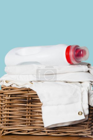 A plastic bottle of liquid laundry detergent resting on top of a neatly folded pile of white clothing in a basket.