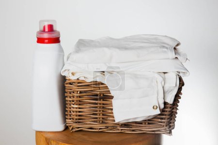 A detergent bottle next to neatly folded white linen in a wicker basket. Represents cleanliness and household chores