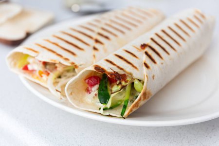 Close-up of wraps with grill marks on plate, filled shawarma at grill pan, durum doner recipe, Fresh veggies and sauce inside.