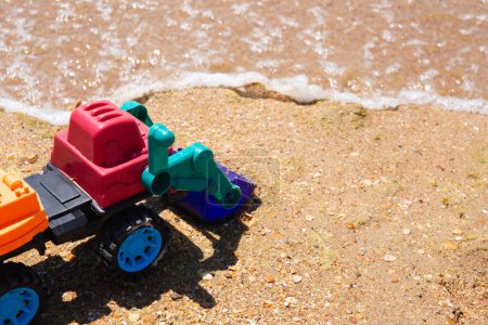 Ein Spielzeugbagger sitzt auf Sand, im Hintergrund Wellen. Es ist bunt, verspielt, Familienurlaub, Entwicklungskrise, Sicherheitsregeln in der Nähe des Meeres