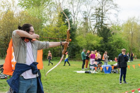Téléchargez les photos : Un homme aime le tir à l'arc à la fête du roi aux Pays-Bas. C'est des vacances heureuses avec plaisir au marché aux puces - Pays-Bas, Amsterdam, 27.04.2023 - en image libre de droit