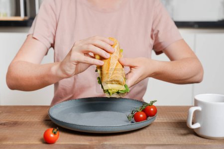 woman making sandwich with baguette and cheese, holding it in hands and preparing to bite, making breakfast, morning routing theme