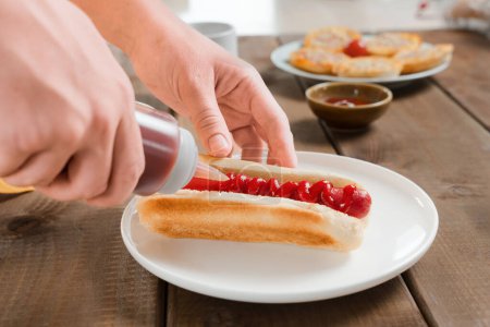 A woman squeeze ketchup from ketchup bottle to a hot dog, a fast food, fast lunch or American breakfast.. Vegan or meat sausage