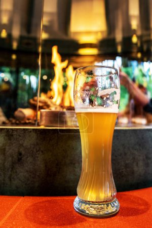 Foto de Un vaso de cerveza ligera en un pub oscuro contra un fuego ardiente - Imagen libre de derechos