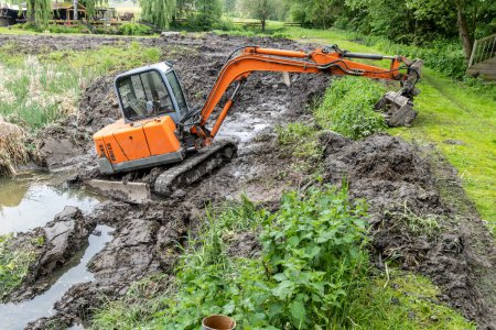 An excavator clears a silted lake, which is overgrown with reeds