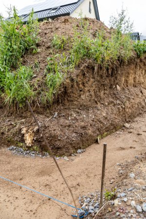 Photo for Earthworks, trench digging. A long earthen trench dug for laying a pipe or foundation. Construction of sewerage and drainage. The trench is silted with clay after the rain - Royalty Free Image