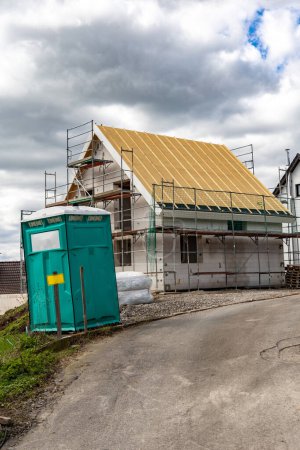 Photo for Construction of new houses in the village. A building under construction and a toilet for builders in the foreground - Royalty Free Image
