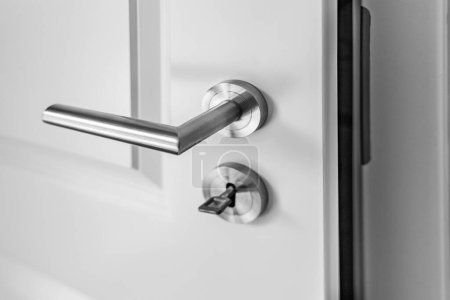 Photo for Close-up of a slightly open white wooden door with a latch handle and a key in the keyhole - Royalty Free Image