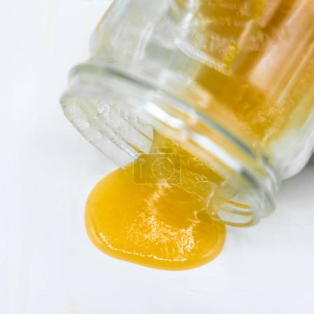 La miel se vierte de un frasco sobre un fondo blanco, primer plano